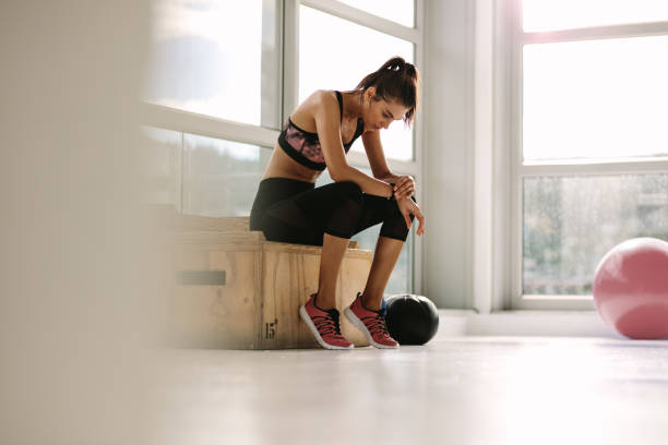 Young woman resting on box after workout at gym. Fitness female taking break after training session in health club.