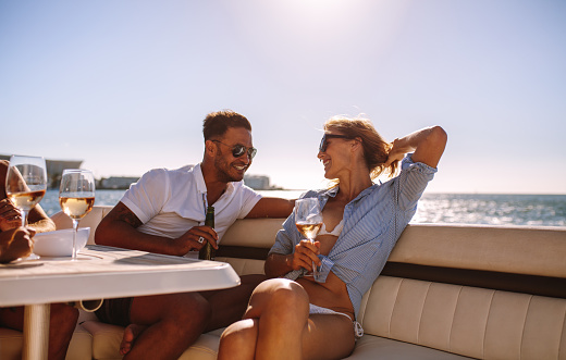 Smiling couple sitting on a boat with drinks. Relaxed young people during a boat party.