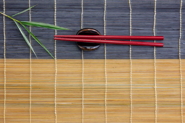 Red chopsticks with holder and bamboo leaves on bamboo mat stock photo