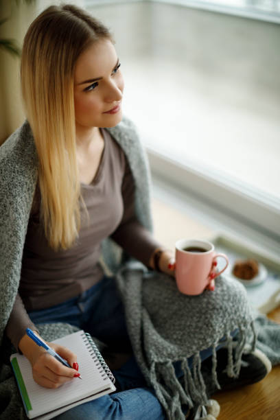 istock Thoughtful young woman sitting on the floor and writting notes 943315782