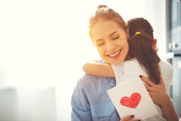 muttertag! kind-tochter gratuliert mütter und gibt ihr eine postkarte - people care surprise love stock-fotos und bilder