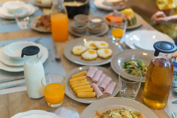 breakfast on table served with  foods,boiled rice,fried egg,sausage,bread,pastries,hot and cold drink,coffee.