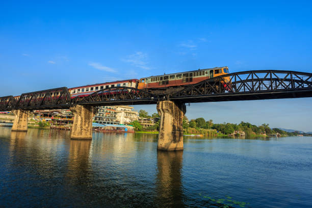 поезд проходит через мост через реку квай, построенный во время второй мировой войны. - burma railway стоковые фото и изображения