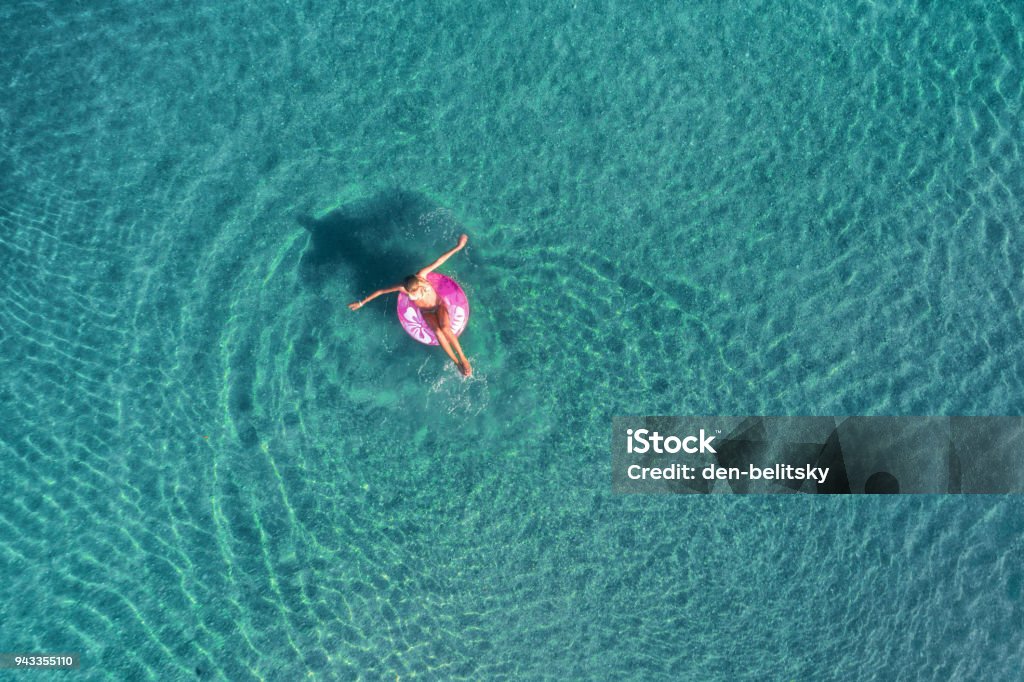 Aerial view of young woman swimming on the pink swim ring in the transparent turquoise sea at sunrise in Thailand. Summer seascape with girl, clear water in the morning. Top view. Travel and holiday Aerial View Stock Photo