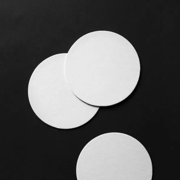 Three blank white beer coasters on black paper background. Responsive design mockup. Top view. Flat lay.