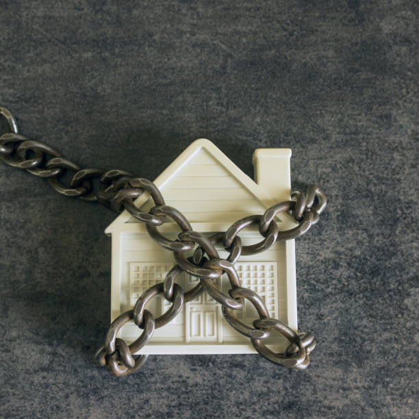 istock Small white house and a decorative chain on a dark background. Concept  -  risks, lose property,  seize, mortgage. 943387040