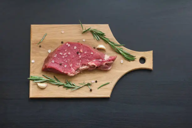 raw beef steak with rosemary, garlic, pepper and salt on cutting board