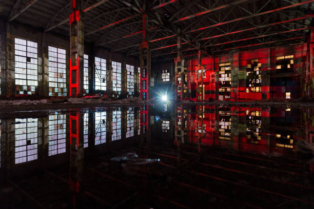 Flooded abandoned large industrial hall illuminated by red lights. Reflection in water. Abandoned Voronezh excavator plant.