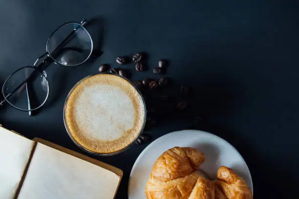 Toviwe, Latte art ,Croissant ,book,glasses and with Roasted coffee on black background in the morning top view and instagram style filter photo vintage tone