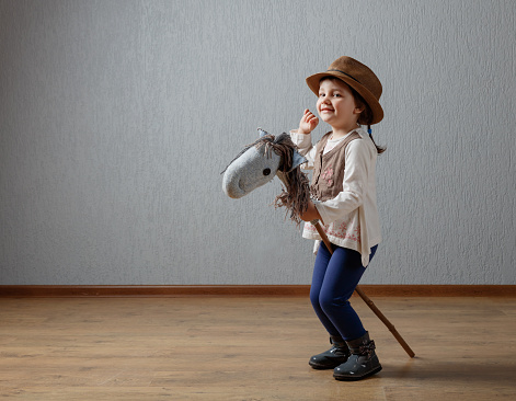 Cute little girl dressed like a cowboy playing with a homemade horse. Expressive facial expressions.
