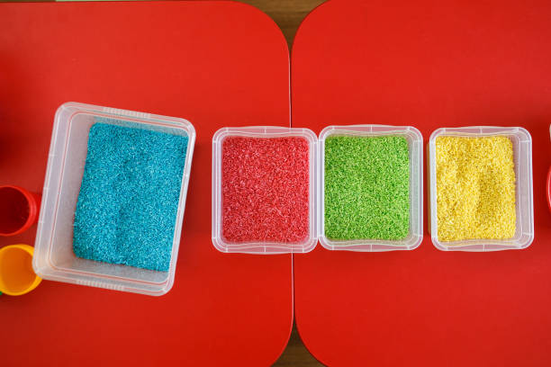 istock Sensory bin for toddlers with colourful rice on red table. Universal educational game 943401262