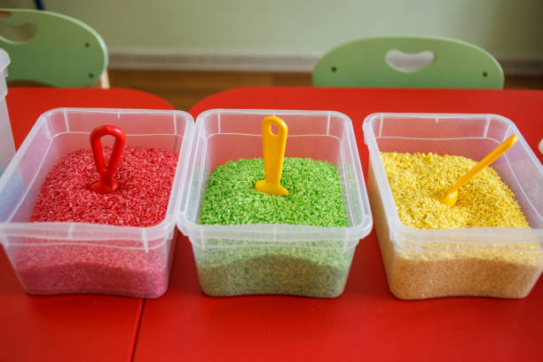 Sensory bin for toddlers with colourful rice on red table