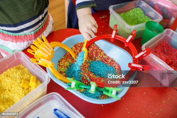 Toddlers Playing With Sensory Bin With Colourful Rice On Red Table Stock Photo - Download Image Now