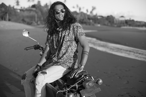 Man sitting on a motorcycle at the beach while using phone