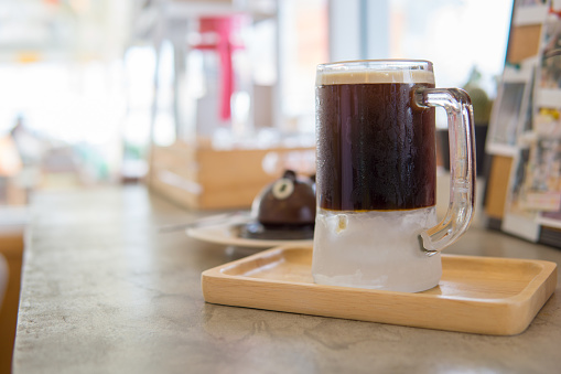 close up of nitro cold brew coffee in big transparent cup with ice at the bottom on the wooden plate with blurred of cafe background.