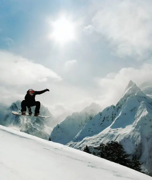 Snowboarder jumping indy grab at rocky mountain background and sunny sky. Young man in extreme freeride action in Dombai, Caucasus mountains