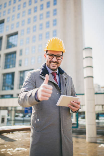 istock Architect in protective helmet showing thumb up in front of office building 943457370