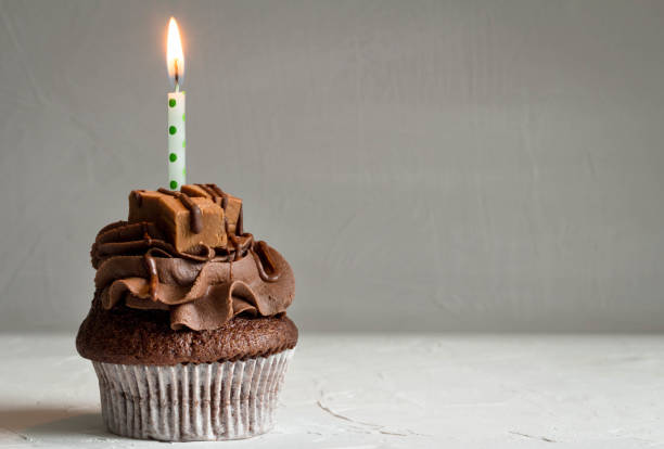 istock One chocolate caramel cupcake with lit candle on dark grey background 943472116