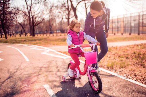 Single mother helping her daughter while learning to ride a bicycle in the park.