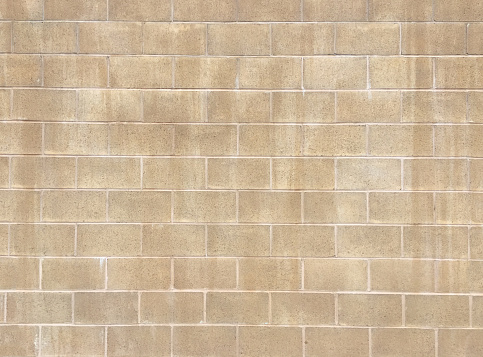 A full frame abstract background of a beige colored brick wall with white color mortar which is old, weathered and stained giving it a rustic grunge textured pattern.