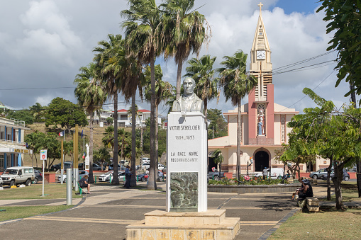 Sainte-Anne, Guadeloupe -February 9, 2018: Main square (Place Schoelcher) in the town Sainte-Anne. A bust of French abolitionist writer Victor Schoelcher and Saint Anne's catholic church in background