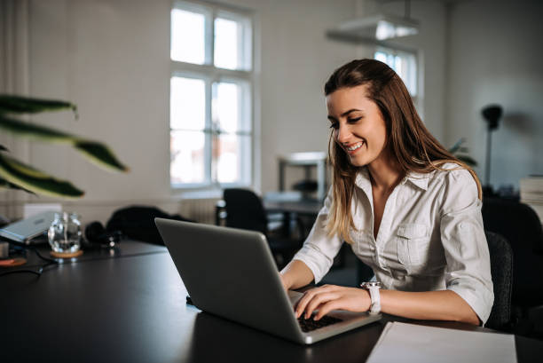 istock Smiling brunette girl working on a laptop at modern office 943494954
