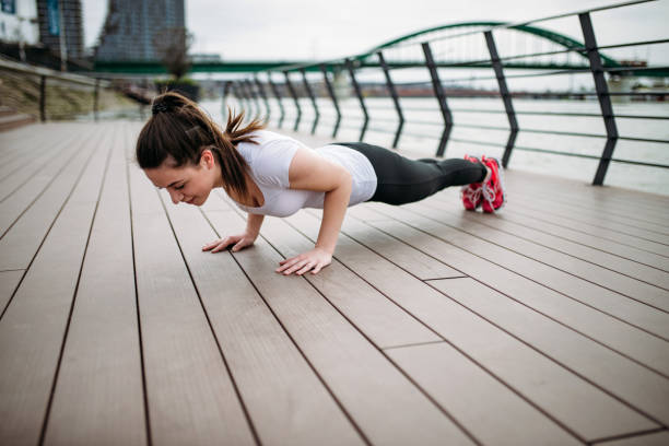 istock Doing push-ups outdoors. Fit girl exercising at city quay. 943495018