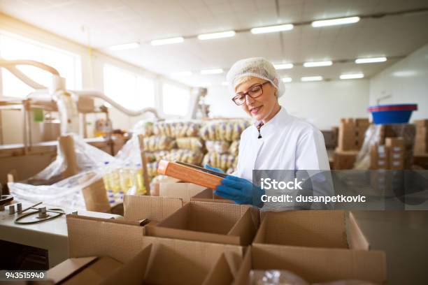 Close Up View Of A Young Female Pleased Worker In Sterile Cloths Packing Finished Food Products In A Boxes In Food Factory Storage Stock Photo - Download Image Now