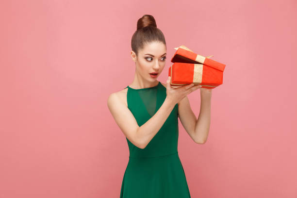 Cunning woman unboxing red gift box looking inside Cunning woman unboxing red gift box looking inside. Expression emotion and feelings concept. Studio shot, isolated on pink background woman stealth stock pictures, royalty-free photos & images