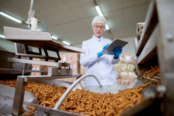 cerrar vista de una snacks de sal stick está procesando a través de una línea de producción en fábrica del alimento mientras que la inspección de una joven trabajadora con una tableta en un paño estéril. - sales manager fotografías e imágenes de stock