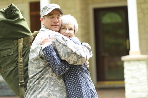 Family welcomes home USA army soldier. Family welcomes home a USA army soldier. Mother excitedly hugs adult son, who wears combat uniform and carries duffle bag. They stand in front of mother's home. proud army mom stock pictures, royalty-free photos & images
