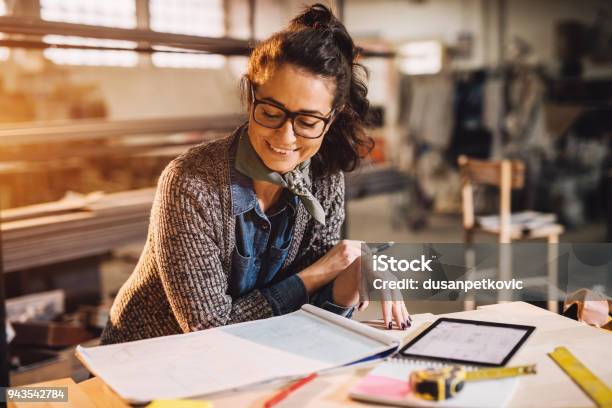 Close Up View Of Charming Smiling Motivated Middle Aged Industrial Female Engineer With Eyeglasses Working With Blueprints And Tablet In The Workshop Stock Photo - Download Image Now