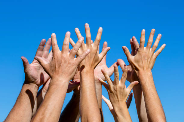 istock Group of people pulling hands in the air in sunlight. Many hands against blue sky background 943581826