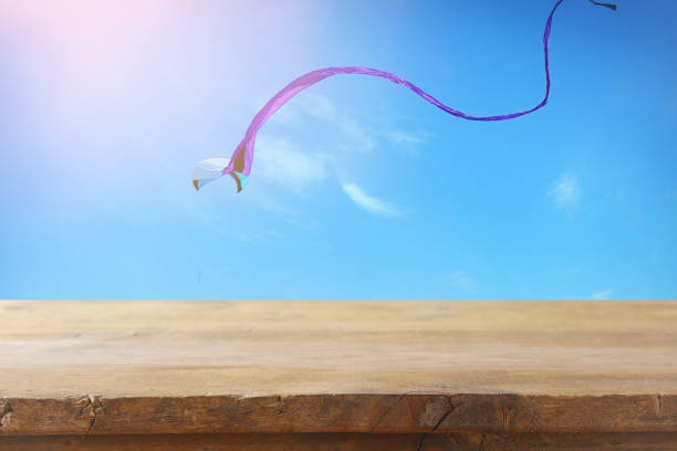 istock Image of empty rustic table in front of Colorful kite flying in the blue sky through the clouds. For product display presentation. 943597932