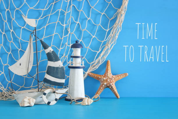 istock nautical concept with white decorative sail boat, lighthouse, starfish, seashells and fishnet over blue wooden table and background. 943602248