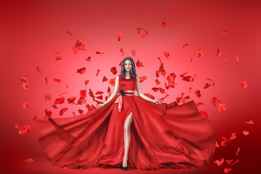 Fashion portrait of young woman in long red dress with flying petals