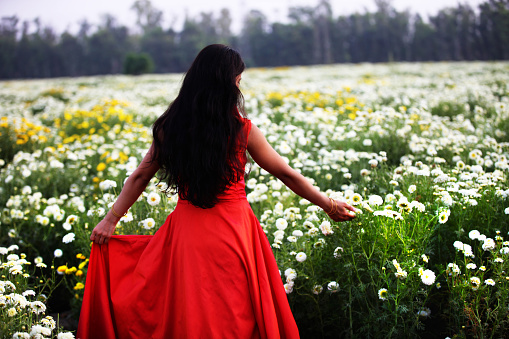 Young woman wearing red color long dress in the chrysanthemum field enjoying spring and fresh air outdoors.