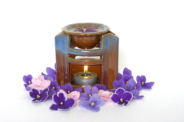 Cut out of aroma bottle diffuser with wooden sticks placed in front of lit brown candles and dry objects for a relaxing session of mindfulness and meditation.