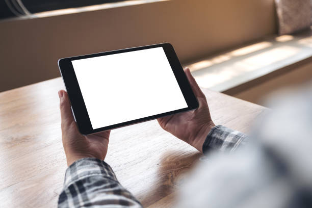 istock Mockup image of hands holding black tablet pc with blank white desktop screen on wooden table 943638660
