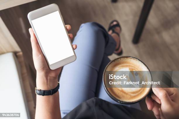 Top View Mockup Image Of A Womans Hand Holding White Mobile Phone With Blank Desktop Screen While Drinking Coffee In Cafe Stock Photo - Download Image Now