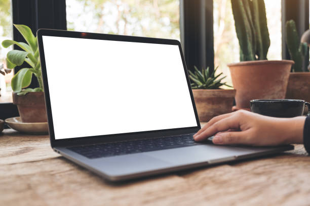 istock Mockup image of hand using and typing on laptop with blank white desktop screen on vintage wooden table in cafe 943638830