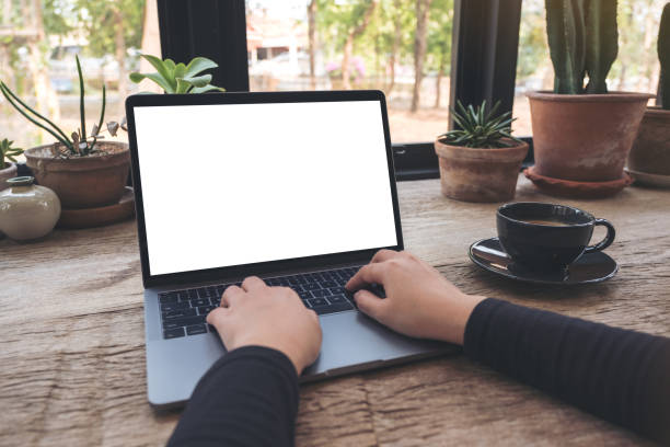 istock Mockup image of hands using and typing on laptop with blank white desktop screen on vintage wooden table in cafe 943638898