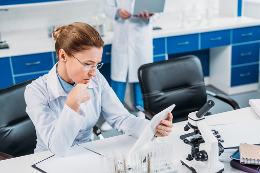 selective focus of female scientist using tablet at workplace with colleague behind in lab