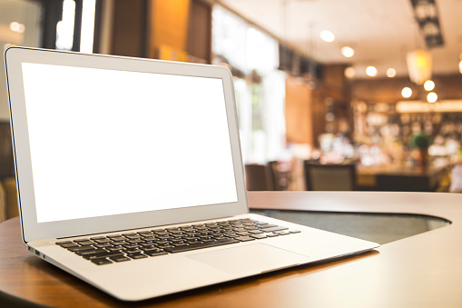 Mockup image of laptop with blank white desktop screen on wooden table in modern cafe with abstract bokeh light image background.