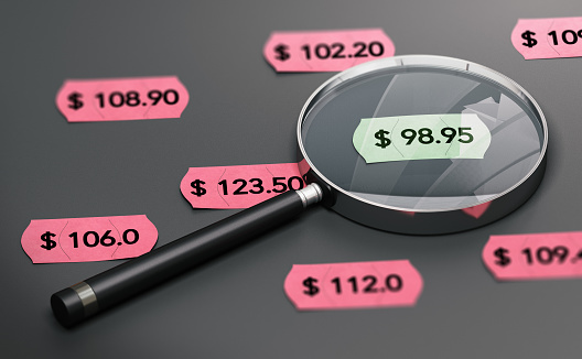 3d illustration of a magnifying glass over black background with price tags and focus on the cheapest one.