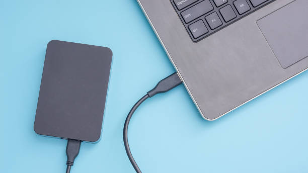 istock Black external hard disk connecting to a laptop on a blue background. 943662880