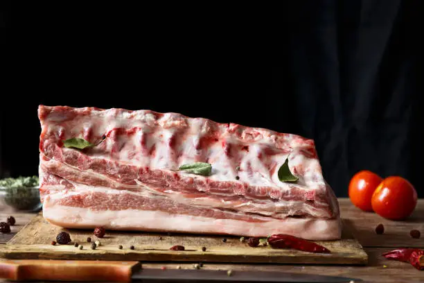 Raw meat of pork with edges lies on a wooden table and a black background with seasonings. Copy space