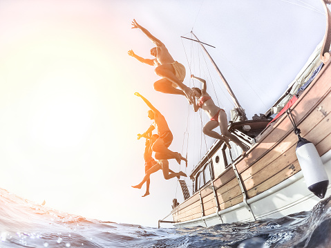 Multiracial young people diving from sailing boat into the sea - Cheerful friends having fun in summer party day - Vacation and friendship concept - Soft focus on right man - Fisheye lens distortion