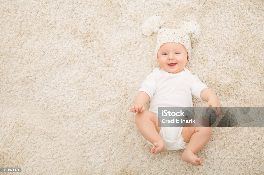 Happy Baby in Hat and Diaper on Carpet Background, Smiling Infant Kid Boy in White Clothing Happy Baby in Hat and Diaper Lying on Carpet Background, Smiling Infant Kid Boy in White Clothing, Child Six Months Old Baby - Human Age Stock Photo
