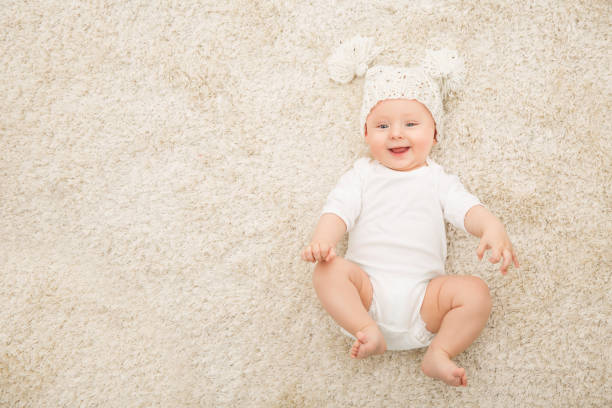 Happy Baby in Hat and Diaper on Carpet Background, Smiling Infant Kid Boy in White Clothing Happy Baby in Hat and Diaper Lying on Carpet Background, Smiling Infant Kid Boy in White Clothing, Child Six Months Old babies only photos stock pictures, royalty-free photos & images
